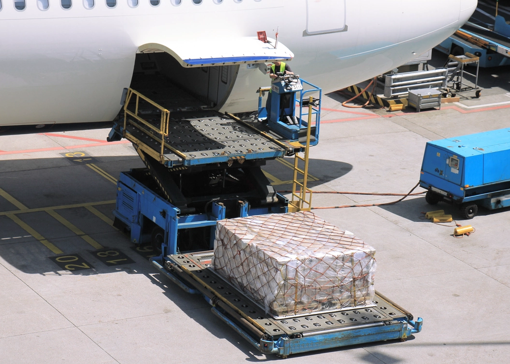 Ground crew loads cargo onto an aircraft using an air cargo loader.