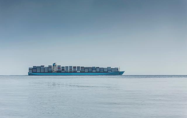 Loaded container ship sailing on calm open water under a hazy blue sky