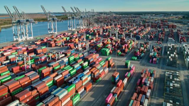 Aerial view of a container port with thousands of stacked shipping containers and gantry cranes beside a river