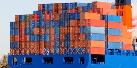 Stern of a container ship loaded with stacked colorful shipping containers against blue sky