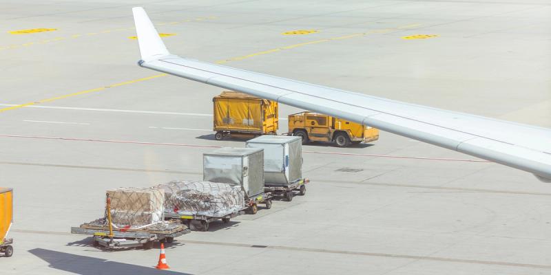 Air cargo pallets and containers on dollies beside an aircraft wing on the tarmac