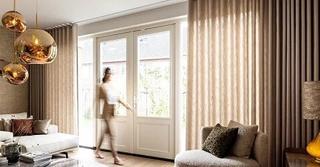 Woman walking through a modern living room with floor-length striped curtains and pendant lights