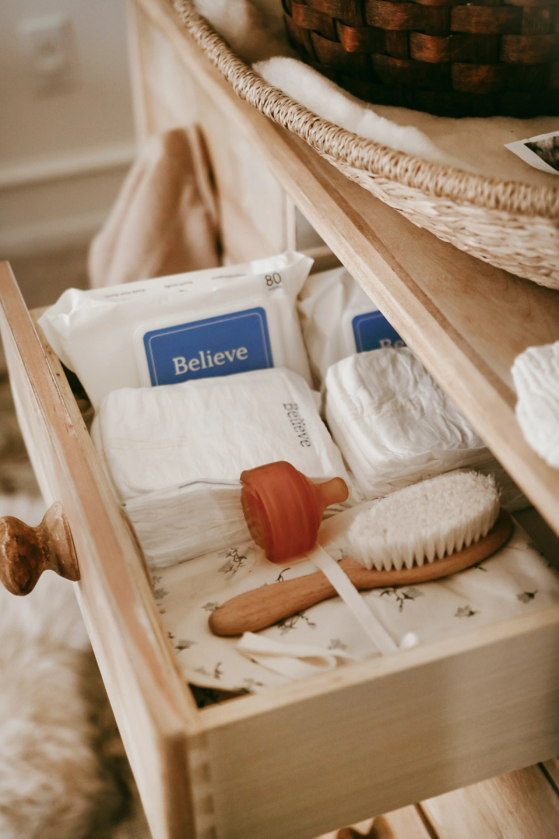 Open wooden changing-table drawer holding Believe diapers, wipes, and a baby brush