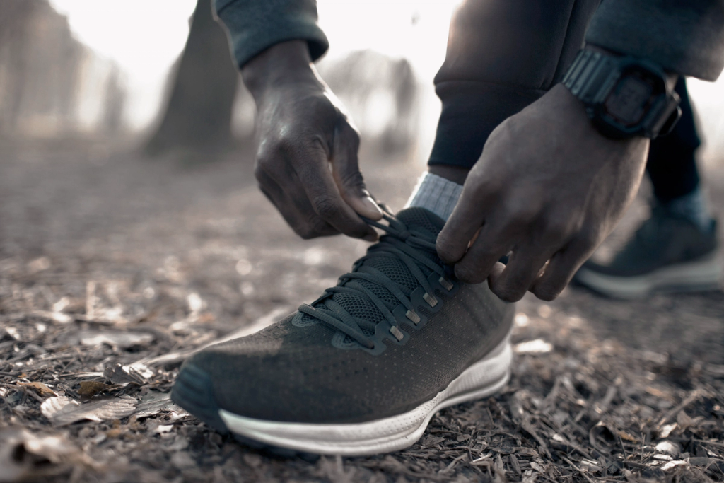Person tying shoelaces on a running shoe outdoors before exercise.