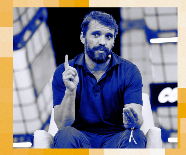 Duotone blue portrait of a bearded man seated, raising his index finger mid-gesture, against an arena backdrop