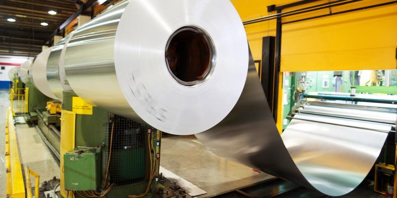 Large coil of rolled aluminum sheet metal on green machinery in a factory with yellow walls