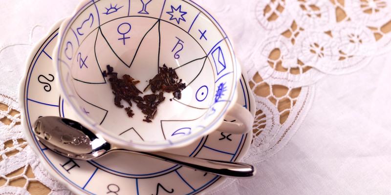 Teacup on a zodiac-symbol saucer with tea leaves in the bottom and a spoon on lace cloth