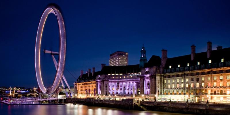 The illuminated London Eye and County Hall reflected on the River Thames at dusk under a deep blue sky