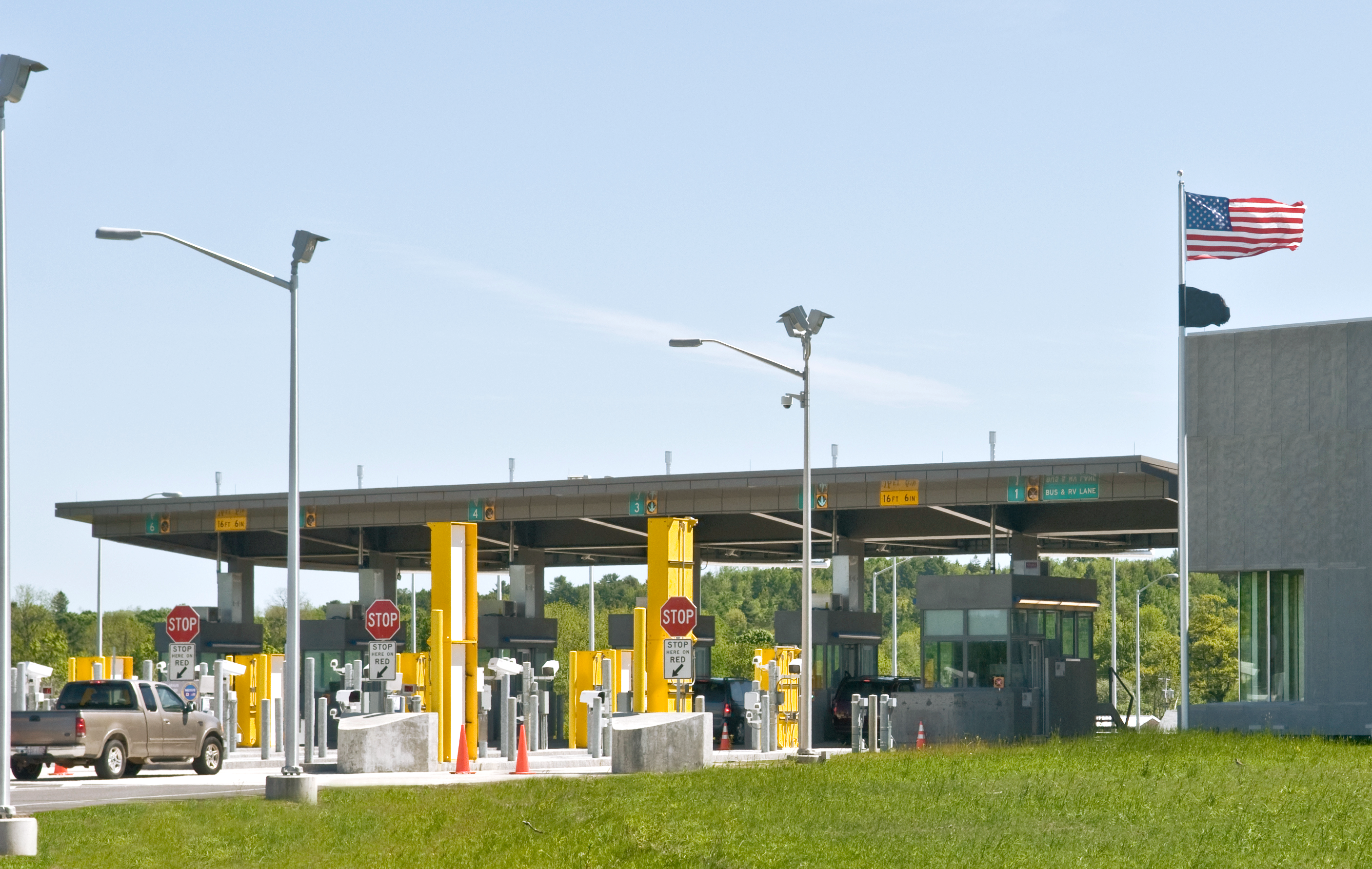 U.S. border crossing checkpoint with numbered inspection lanes, stop signs, and an American flag flying beside the station