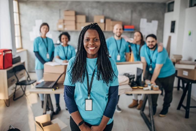 Smiling woman in teal volunteer shirt and lanyard with diverse team in matching shirts among boxes