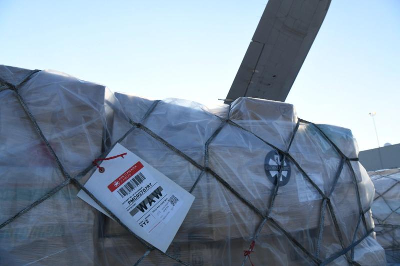 Plastic-wrapped GlobalMedic relief cargo pallet in a cargo net with an Air Canada Cargo WAW tag, beside an aircraft wing