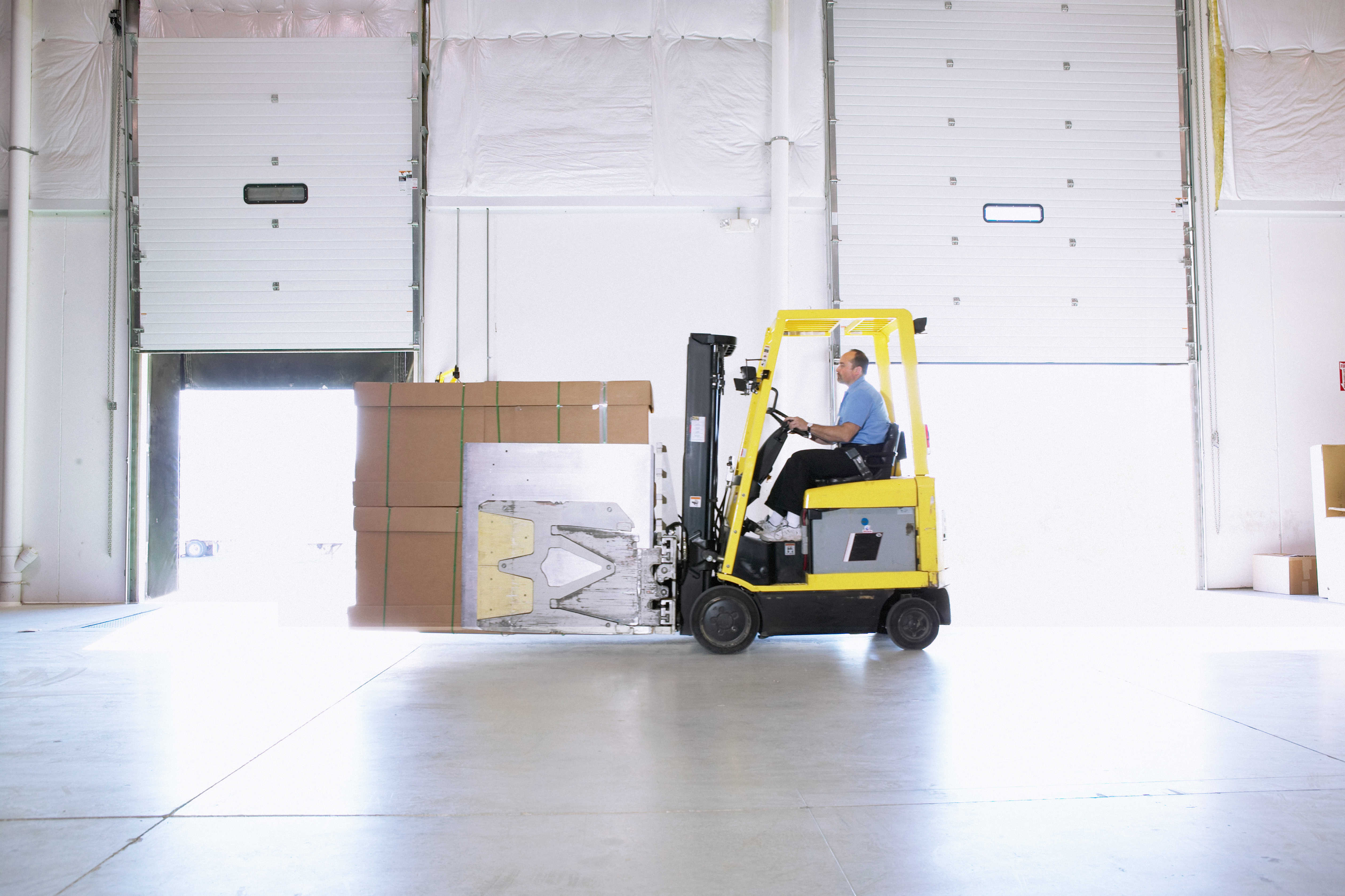 Forklift operator transporting stacked cardboard boxes in a warehouse.