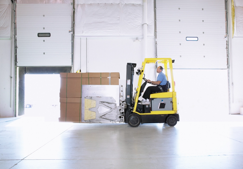 Forklift operator transporting stacked cardboard boxes in a warehouse.