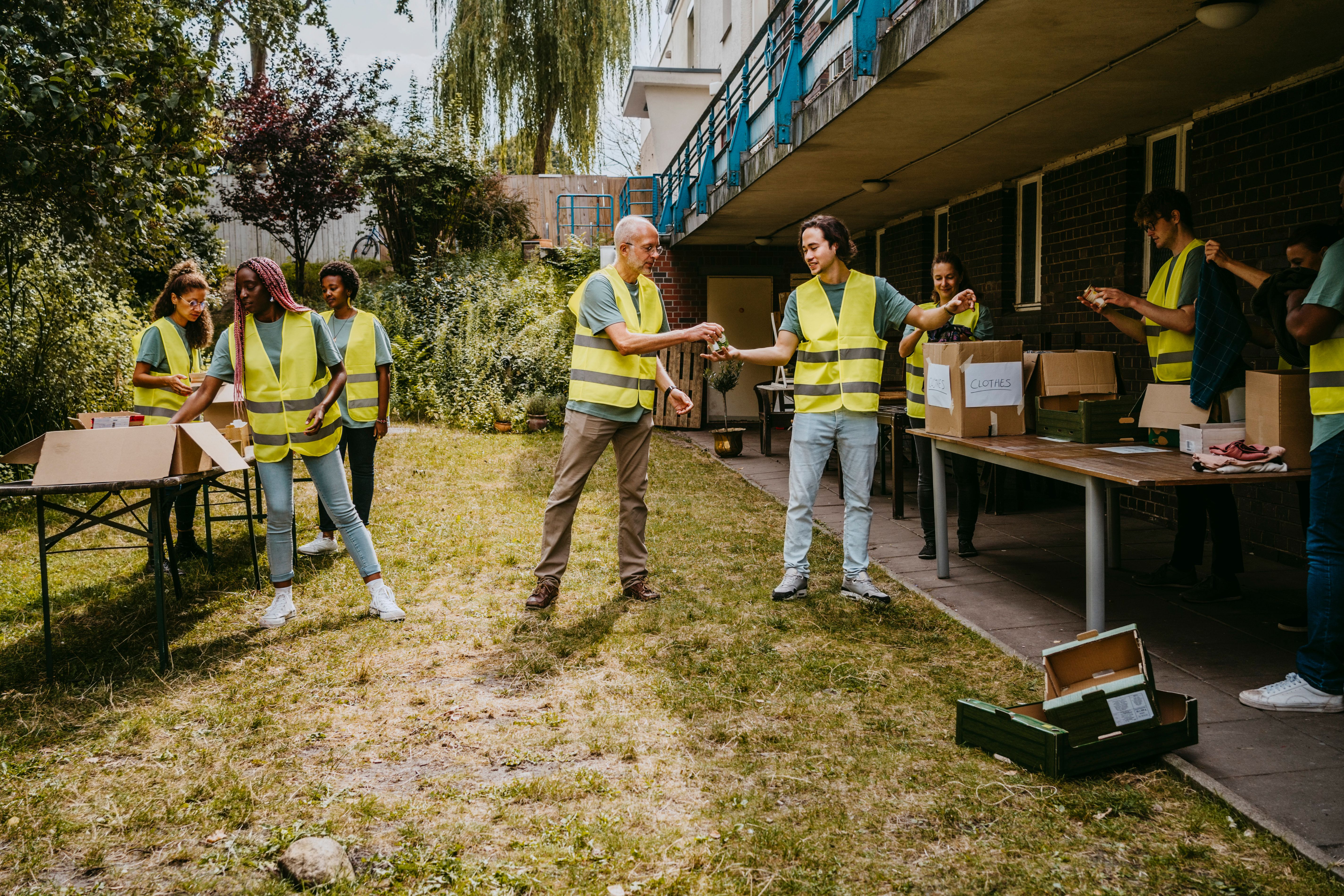 Group of volunteers in safety vests sorting and distributing cardboard boxes during outdoor charity activity.
