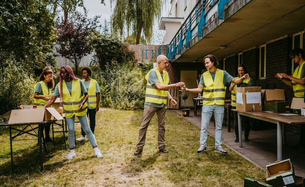 Group of volunteers in safety vests sorting and distributing cardboard boxes during outdoor charity activity.