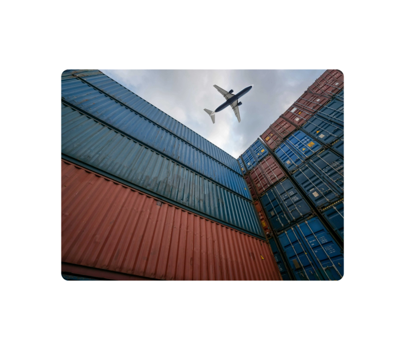 Low-angle view of stacked shipping containers framing a passenger jet flying overhead, evoking combined ocean and air freight