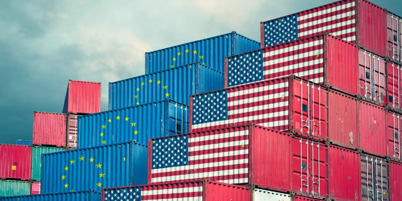 Stacked shipping containers painted with US and European Union flags against a grey sky