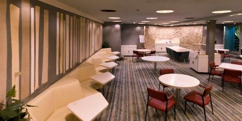 Empty corporate lounge with white booth seating, round tables, and red chairs on patterned blue carpet