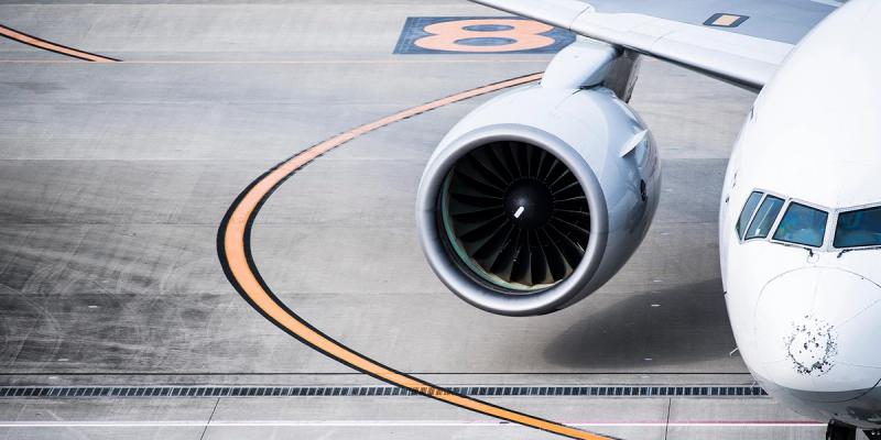 Overhead view of a parked white airliner's nose and jet engine on a marked airport taxiway