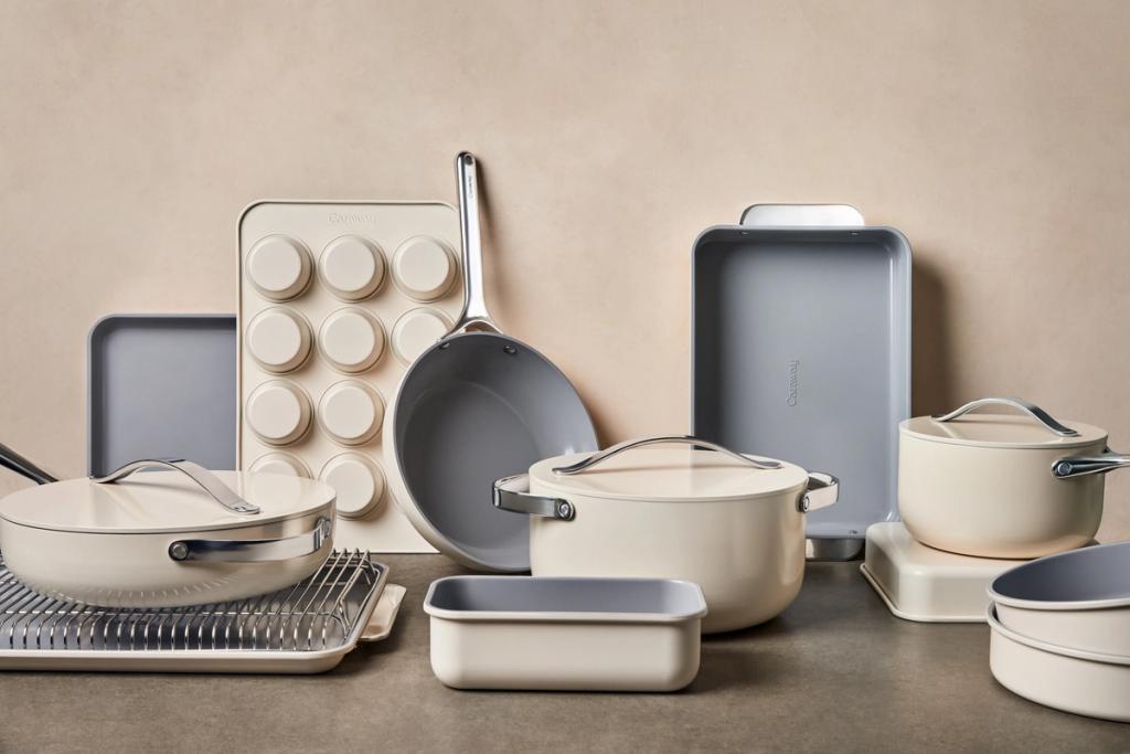 Cream and gray Caraway cookware and bakeware set arranged against a tan wall