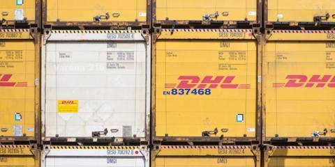 Stacked yellow DHL shipping containers showing the red DHL logo and container ID numbers.