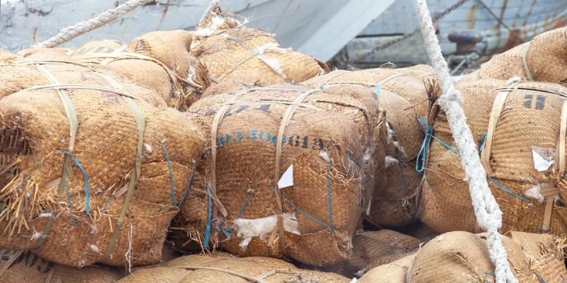 Roped bales of raw cotton wrapped in woven burlap stacked on the deck of a boat