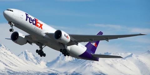 White FedEx Express Boeing 777 freighter taking off above snow-capped mountains