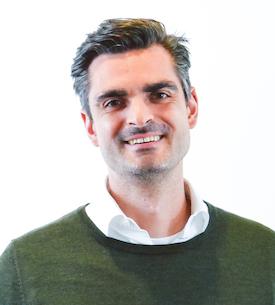 Headshot of a smiling man with short dark hair wearing an olive sweater over a white collared shirt.