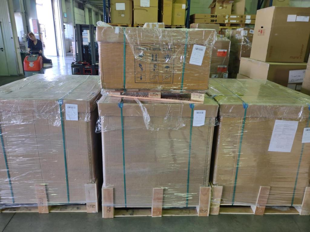 Large shrink-wrapped cardboard freight crates strapped on pallets in a warehouse, worker on a pallet jack behind