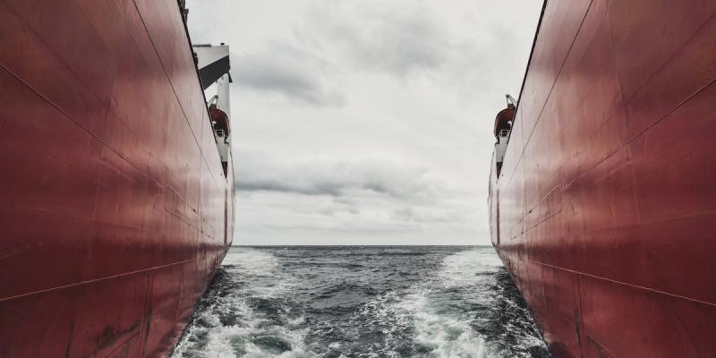 View between the red hulls of two ships, ocean and cloudy sky framed in the narrow gap