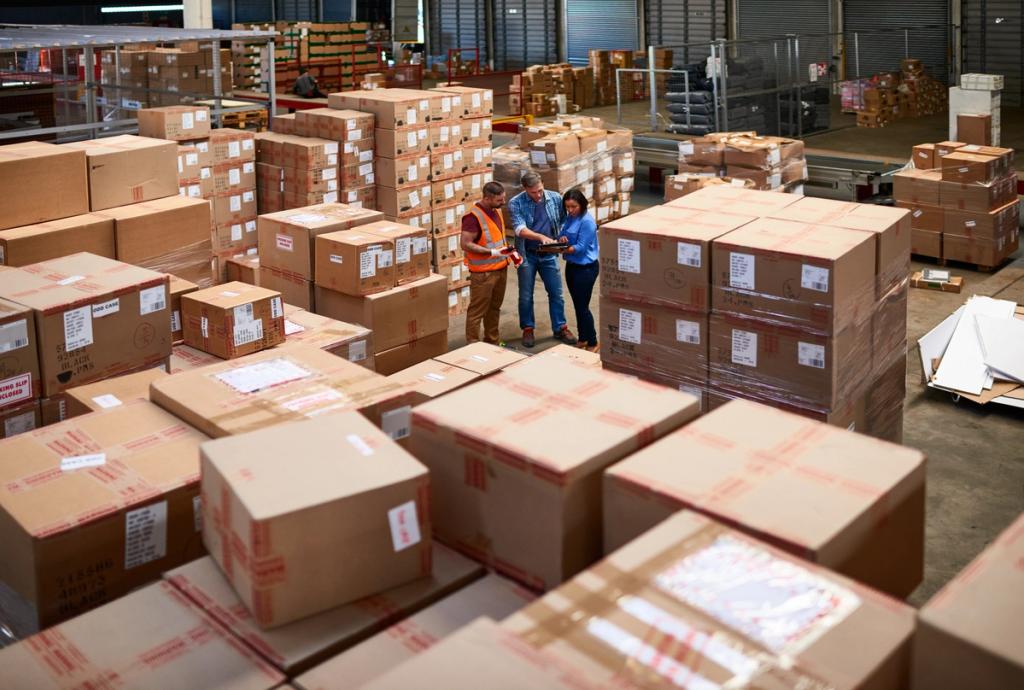 Three workers in safety vests reviewing a tablet amid a warehouse floor crowded with stacked cardboard shipping boxes