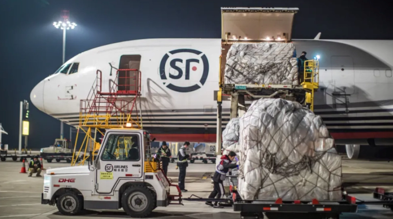 SF Airlines cargo jet being loaded with palletized freight by workers and a tug at an airport tarmac at night