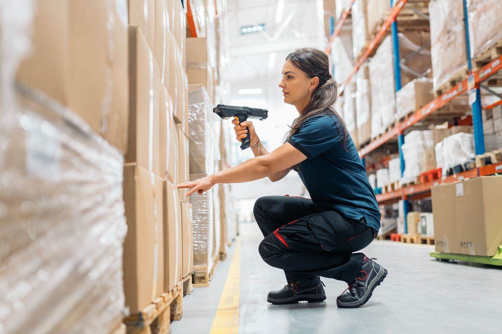 Warehouse worker scanning a product box on a shelf using a barcode scanner.