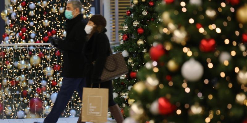 Two masked shoppers walk past brightly lit Christmas trees decorated with red and gold ornaments