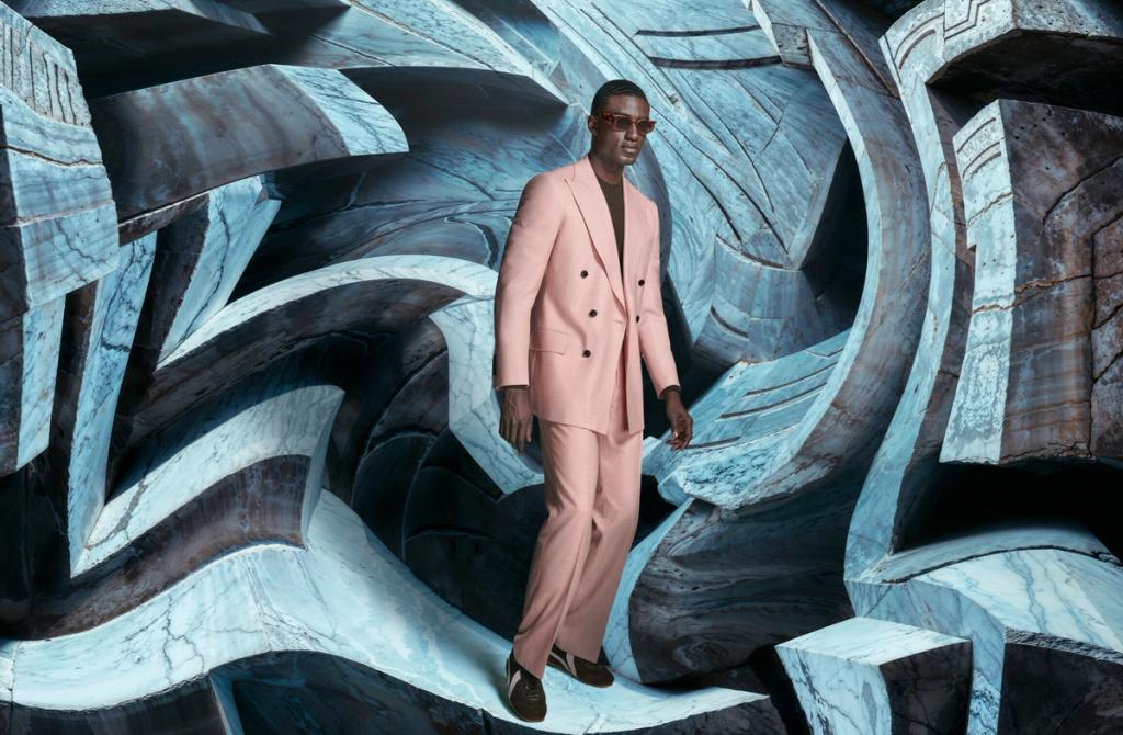 Man in a pink tailored suit and sunglasses walking through a blue stone sculptural set