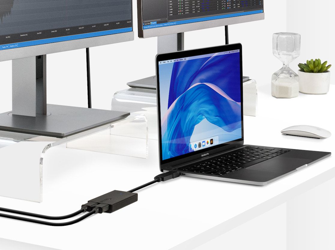 MacBook on a white desk connected to dual monitors via a Plugable docking adapter