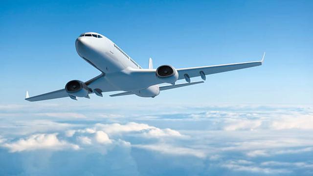 White passenger jet airliner climbing through a clear blue sky above a layer of clouds