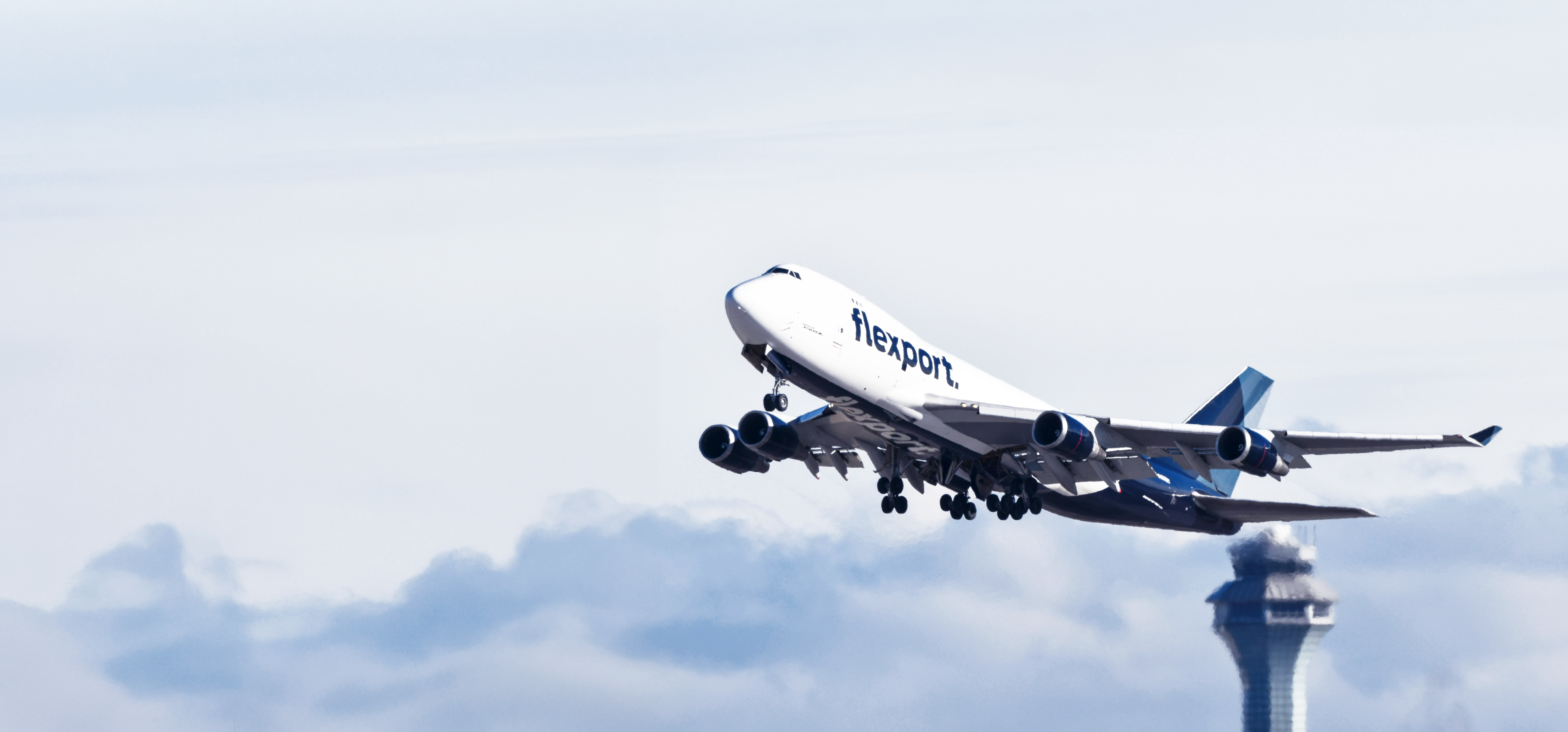 Flexport-branded Boeing 747 cargo jet taking off past an airport control tower