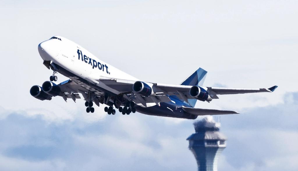 Flexport-branded Boeing 747 cargo jet taking off past an airport control tower