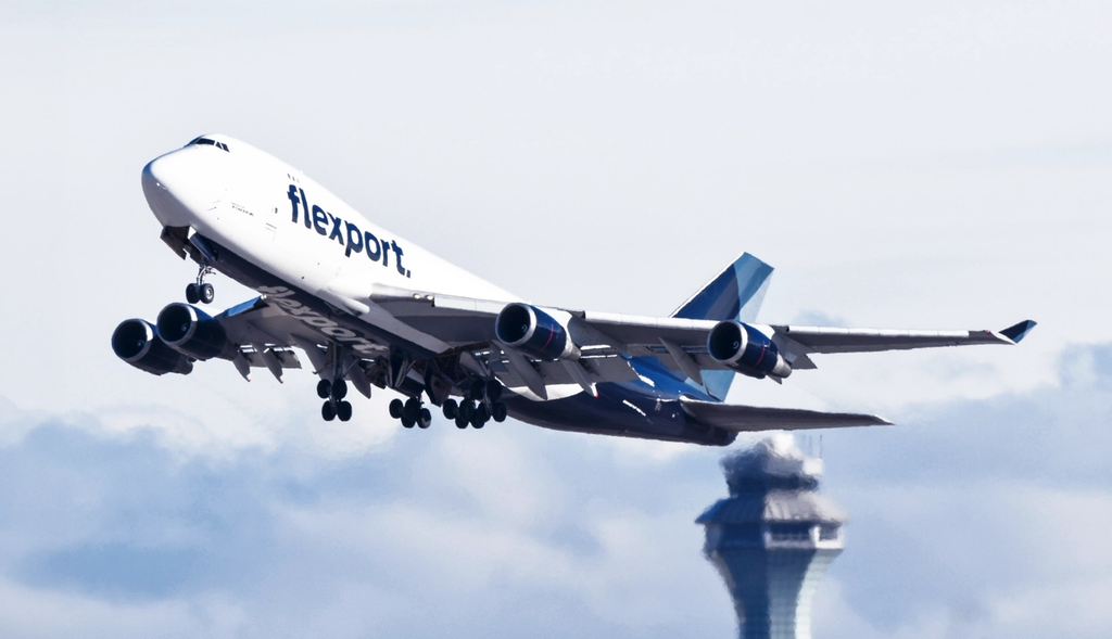 Flexport-branded Boeing 747 cargo jet taking off past an airport control tower
