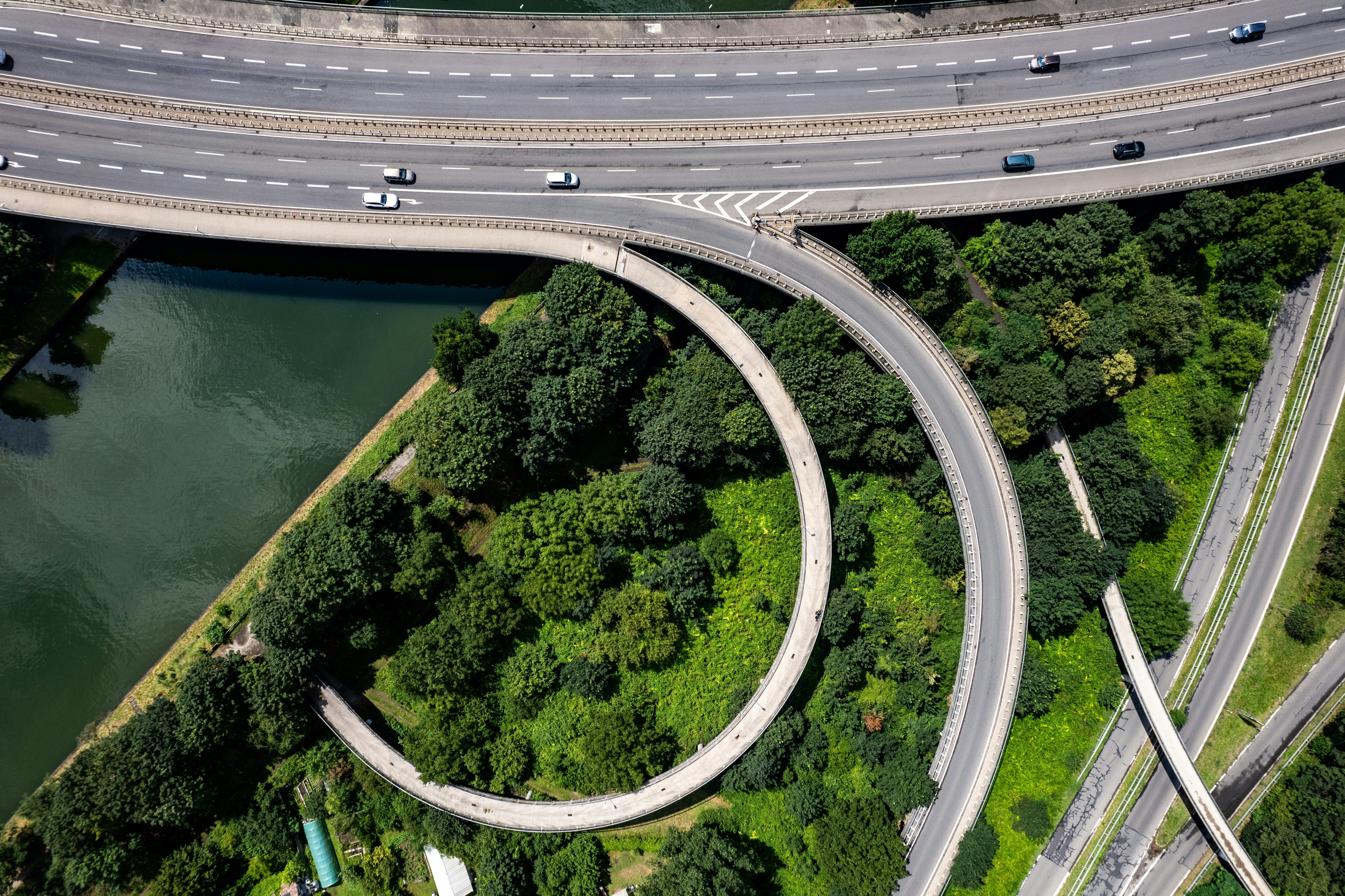 Aerial view of elevated highway interchange with curved ramps crossing over dense forest and water.