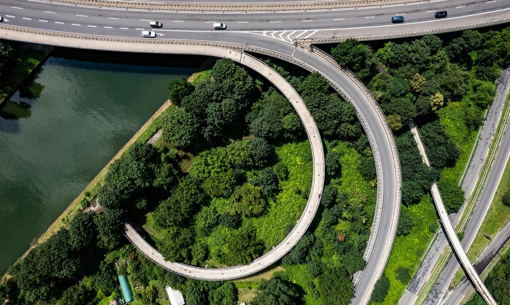 Aerial view of elevated highway interchange with curved ramps crossing over dense forest and water.