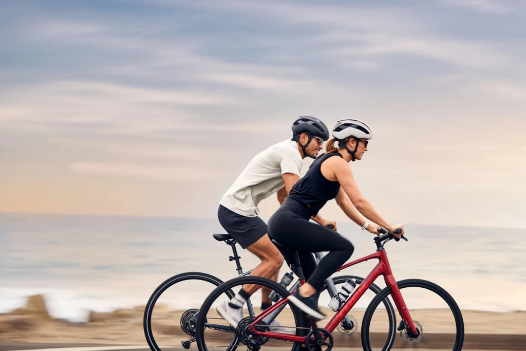 Two cyclists riding together on a tandem bicycle along a beach.