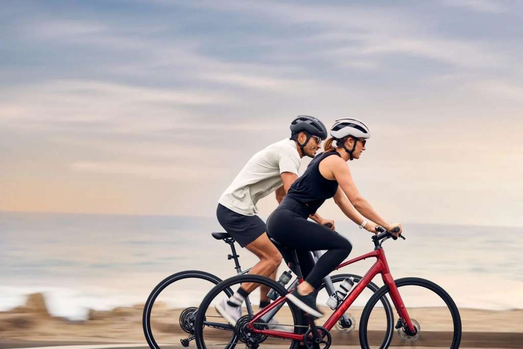Two cyclists riding together on a tandem bicycle along a beach.
