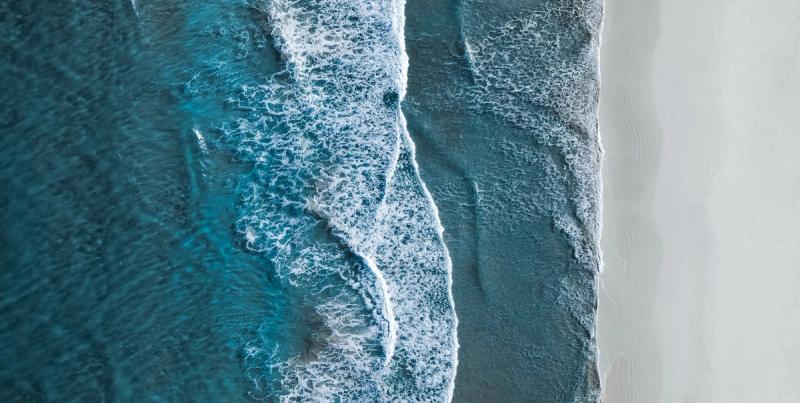 Aerial view of turquoise ocean waves rolling onto a pale sandy beach