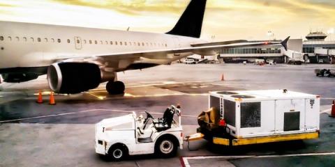 White passenger jet at an airport gate at dusk with a tug and ground service unit on the apron