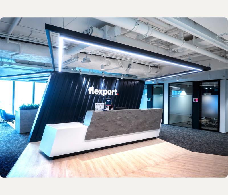 Flexport office reception desk with the Flexport wordmark lit on a dark container-clad wall