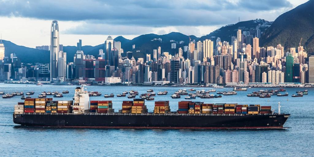 Container ship sailing past the Hong Kong skyline of dense high-rises and harbor boats
