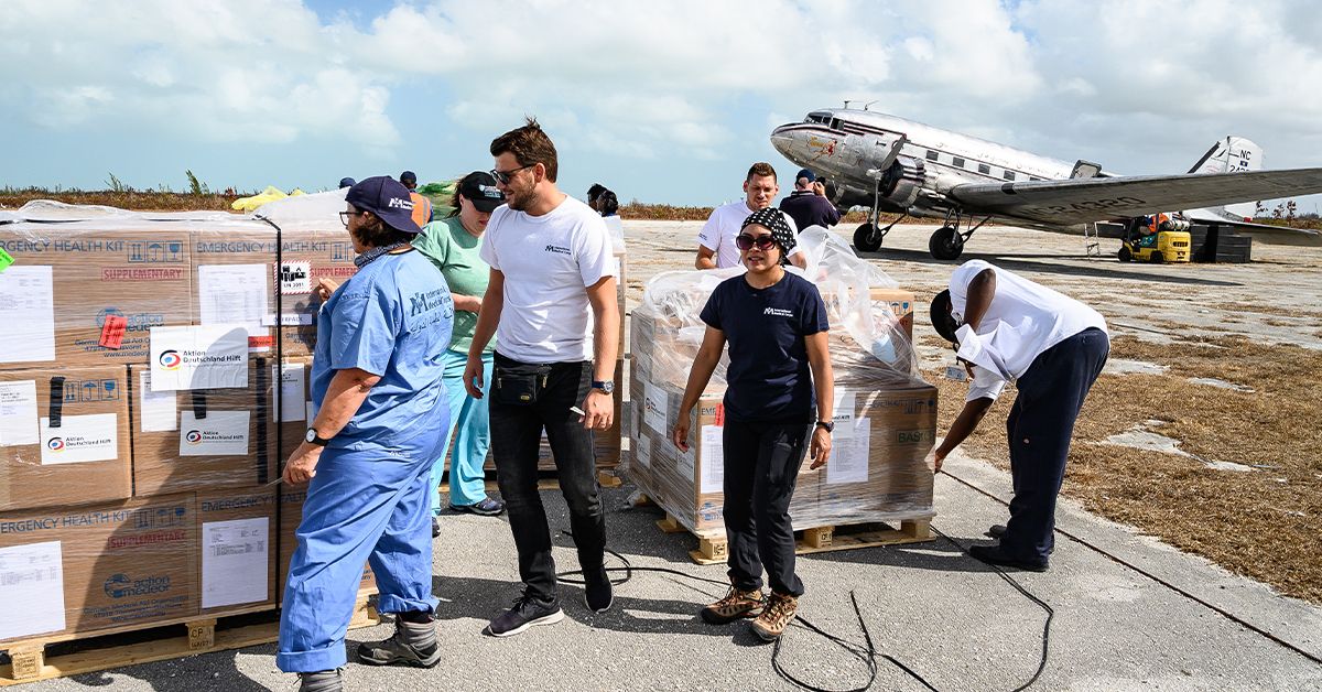 Aid workers unload pallets of emergency health kits beside a vintage cargo plane on an airstrip