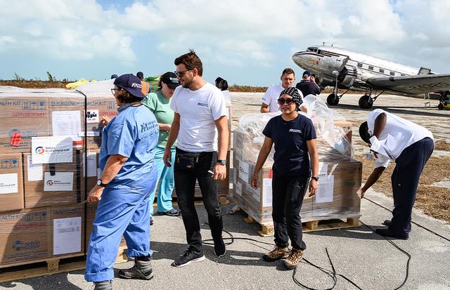 Aid workers unload pallets of emergency health kits beside a vintage cargo plane on an airstrip